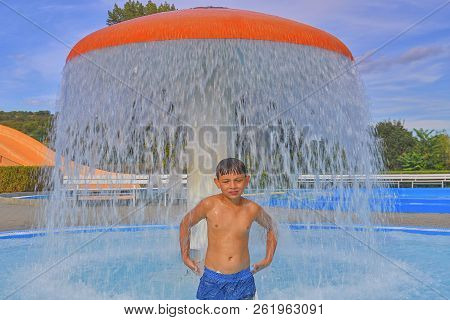 Little Boy In The Small Swimming Pool. Boy Taking Shower In Water Park. Boy Standing Under Sprinkler