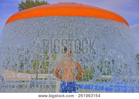 Happy Little Boy Enjoying Summer Day In The Swimming Pool. Boy Standing Under Sprinkler In Spray Poo