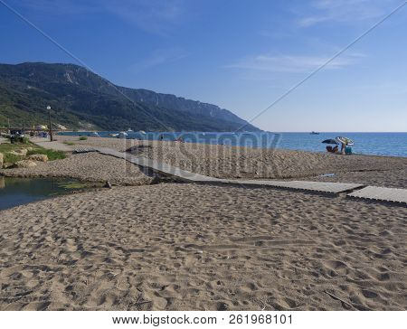 Greece, Corfu, Agios Georgios, September 23, 2018: View On Sea Shore Wooden Promenade With Sand Beac