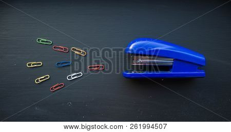 A Stepler And Colored Clips On Black Background