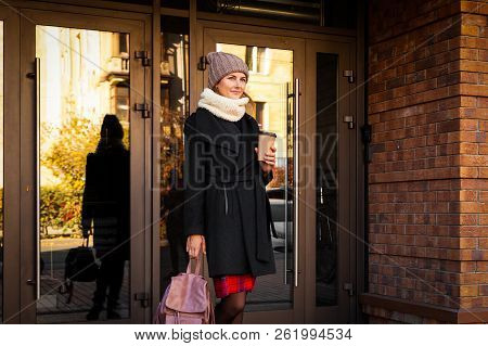 Young Female Student In Warm Autumn Clothes Coming Out Of The House With A Backpack With Books And A