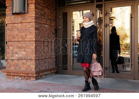 Young Female Student In Warm Autumn Clothes Coming Out Of The House With A Backpack With Books And A