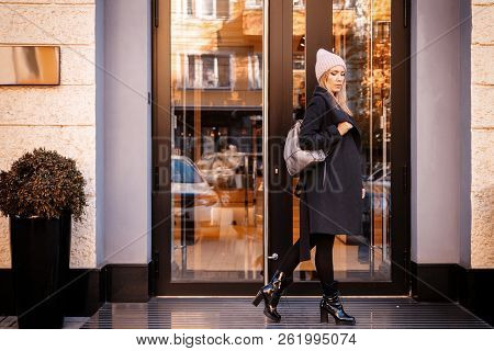 Young Female Student In Warm Autumn Clothes Coming Out Of The House With A Backpack With Books  Arou