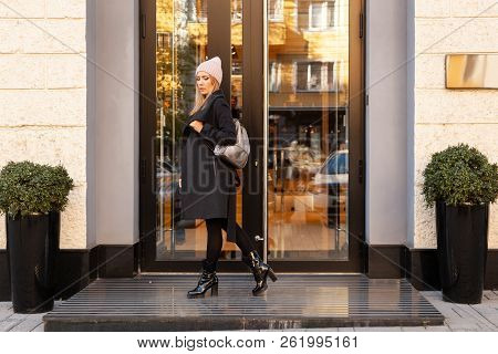 Young Female Student In Warm Autumn Clothes Coming Out Of The House With A Backpack With Books  Arou