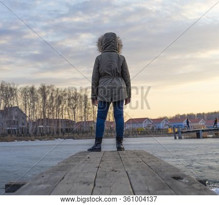 Unrecognizable Girl Standing At Quay By Blue Frozen Lake Surface. Back View, Copyspace. Pensive Kid 