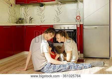 Caucasian Family Sit On Floor In Kitchen.