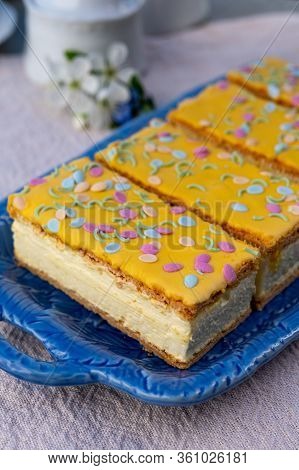 Four Tompouce Cakes With Whipped Cream And Yellow Icing Served In Sunny Spring Garden