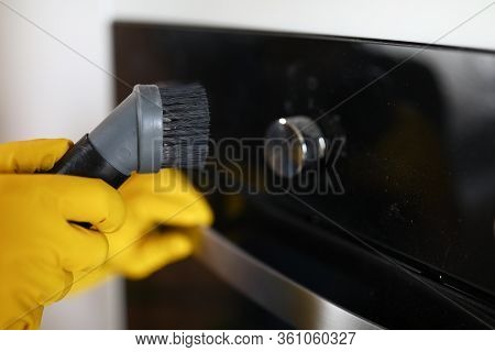 Close-up Of Persons Hand Cleaning Cookstove Display With Nozzle Of Vacuum Cleaner. Male In Protectiv