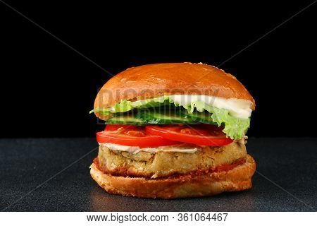 Fresh Tasty Vegan Burger On Black Isolated Background. Tomato, Onion, Vegan Mayonnaise. Vegan Chickp