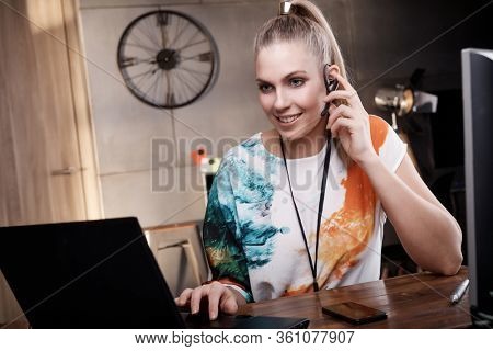 Young woman sitting at desk, using laptop computer and headphone to communicate.
