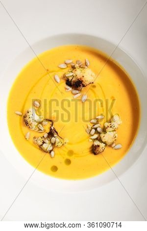 Pumpkin soup in white bowl. Served main course close up. Vegetable cream soup decorated with seeds. Restaurant food portion, main course. Vegetarian supper. Dinner, gourmet meal in plate