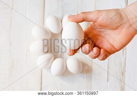 A White Chicken Egg Lying In A Man’s Hand, Shot On A White Painted Wooden Surface. Background For Li