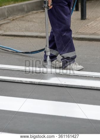 Details With A Road Worker Painting A Crosswalk On A City Street.