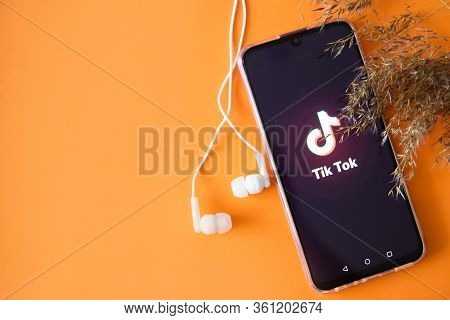 Tver, Russia-april 9, 2020, The Tik Tok Logo On A Smartphone Screen On Orange Background With Headph