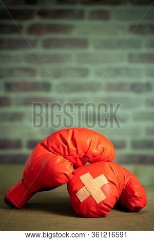 Red Boxing Gloves On Wooden Table And Brick Wall At The Sport Gym. Adhesive Plaster Across Each Othe