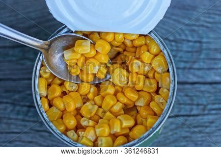 Open Tin Can With Yellow Tinned Corn And A Small Metal Spoon On A Gray Table