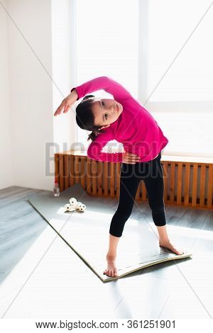 Little Girl Is Doing Back Tilt Standing Workout At Home. Cute Kid Is Training Onon A Mat Indoor Indo