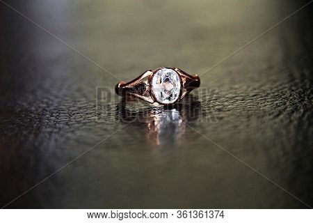 A Ring Of Yellow Melall With A White Shiny Stone Is Reflected On A Shiny Black Background