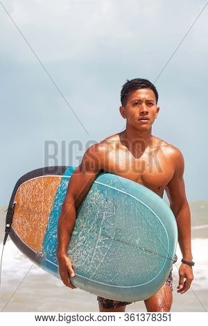 Young Handsome Man Wet All Over Body,walking On The Beach,holding Serf Board With Right Hand.