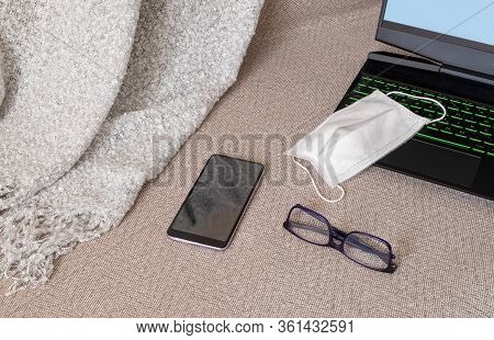 A Laptop, A Medical Mask, Glasses And A Smartphone On A Sofa With A Plaid. Work Or Study From Home, 