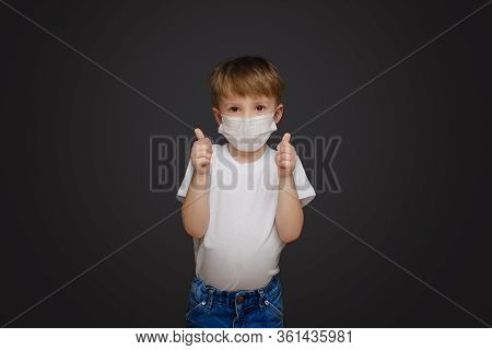 Little Boy On A Gray Studio Background In A Medical Mask Holds Thumbs Up