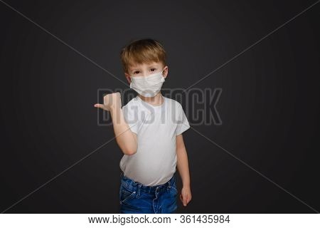 Little Boy On A Gray Studio Background In A Medical Mask, In A White T-shirt And Blue Jeans