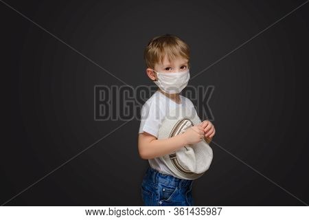 Little Boy On A Gray Studio Background In A Medical Mask With A Hat In His Hands