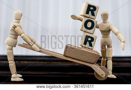 Ror Word On Cubes Standing In Wheelbarrow. A Wooden Man Passes Them To The Second Person. Business C