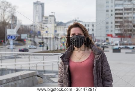 Woman Of European Appearance In A Black Medical Mask On Her Face From The Coronavirus Looks At The B