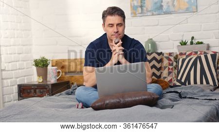 Stay at home and work in home office - Casual man sitting on bed working online from home with laptop computer.