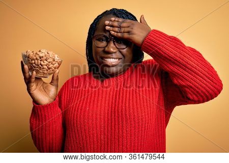 Young african american plus size woman with braids holding bowl with healthy peanuts stressed with hand on head, shocked with shame and surprise face, angry and frustrated. Fear and upset for mistake.