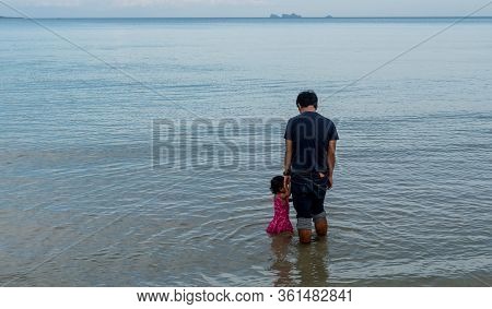 Father And Daughter Standing In Shallow Water With Island In The Background In Thailand On The Gulf 