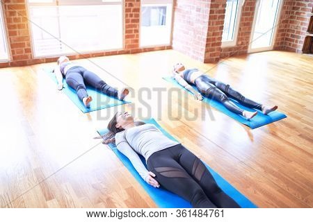 Young beautiful group of sportswomen smiling happy practicing yoga. Lying down doing corpse pose at gym