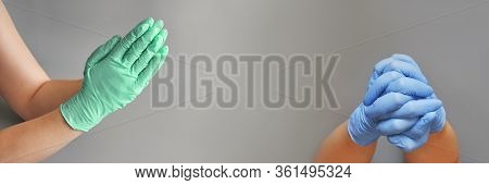 Hands Clasped In Blue And Mint Glove. Grey Background