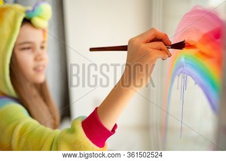 Brush. Stay Home. Girl In Kigurumi Unicorn Draws The Rainbow On The Window. Flashmob Chasetherainbow
