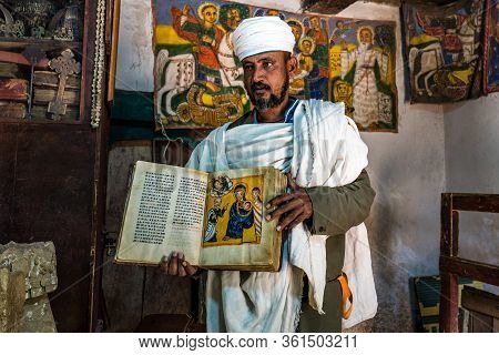 Yeha, Ethiopia - Feb 10, 2020: An Orthodox Priest Shows A Painted Holy Bible From The 14th Century I