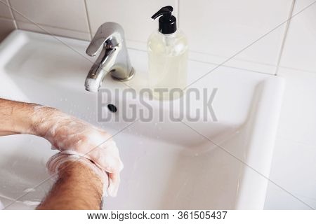 Man Cleaning His Hands Using Liquid Disinfectant Soap And Water In Bathroom.