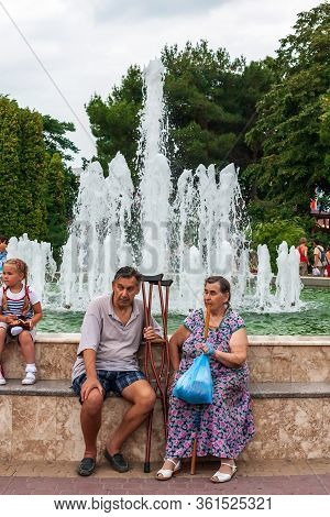 Anapa, Russia - July 26, 2017: Aged Disabled People Sit Together Outdoors By Fountain On Sea Embankm