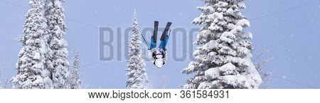 a Freerider in bright gear jumps between Christmas trees with a backflip element. prof skier in a be