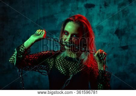 Close Up Portrait Of Beautiful Sexy Witch With Halloween Makeup. Red And Black Face Painting. Chain 