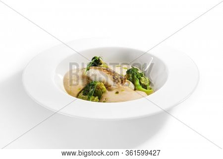 Sea cod fillet close up. Served cuisine. Dish with fish and baked broccoli puree ingredients in white plate isolated. Luxury culinary. Restaurant food portion, delicious supper, main course