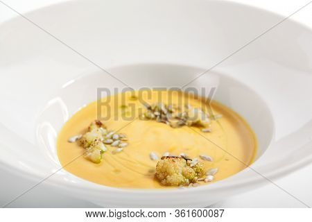 Pumpkin soup in white bowl. Served main course close up. Vegetable cream soup decorated with seeds. Restaurant food portion, main course. Vegetarian supper. Dinner, gourmet meal in plate