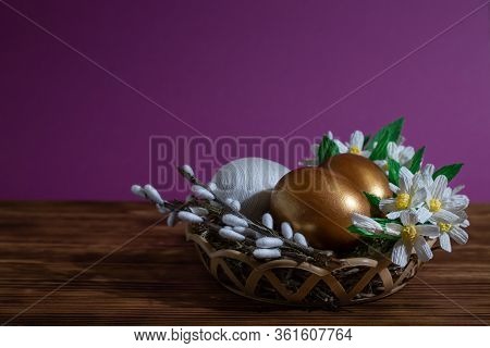 Easter Eggs In Basket Filled With Straw And Yellow Flowers And Willow. Preparation For Holiday. East