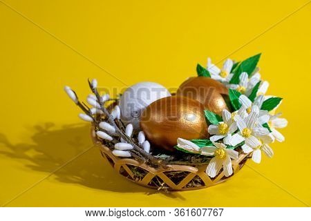Easter Eggs In Basket Filled With Straw And Yellow Flowers And Willow. Preparation For Holiday. East