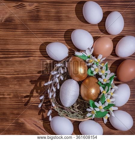 Easter Eggs In Basket Filled With Straw And Yellow Flowers And Willow On Wooden Rustic Vintage Backg