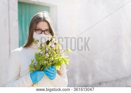 Girl Wearing Medical Mask, Is Looking With Hope And Holding A Branch Of Blooming Twigs Of Apricot. C