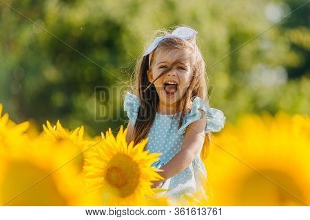 Little Cheerful Girl In A Field Of Yellow Sunflowers. Child And Sunflower, Summer, Nature And Fun. S