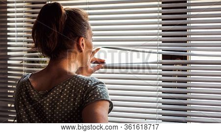COVID-19 Quarantine mental health. Woman self isolated at home pensive looking out of window thinking of relationship, employment, coronavirus. 