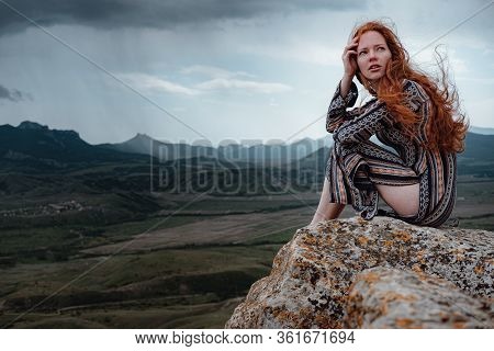 Ginger Woman Sits On A Cliff And Looks At An Impending Storm