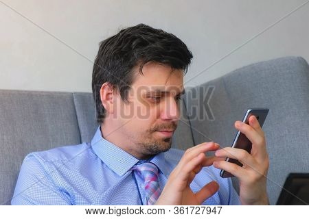 Portrait Of Man Working On Laptop Typing Message Smartphone Sitting On Couch At Home. Distant Work O